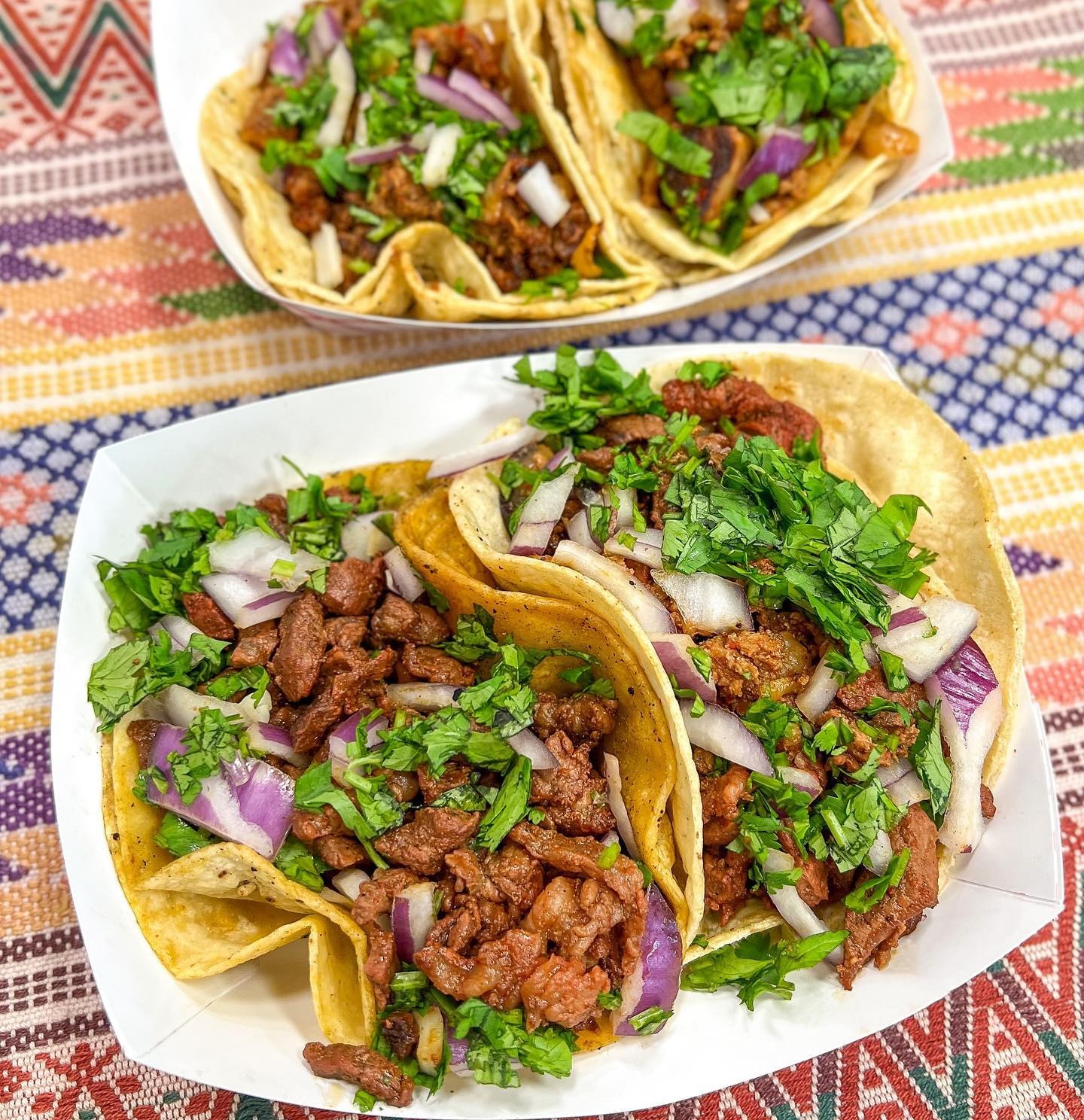 Two trays of arrachera street tacos topped with onion and cilantro on a striped blanket