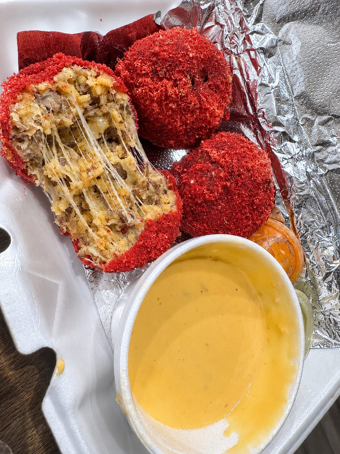 Hot Cheeto birria balls cut open to show melted cheese, with a cup of nacho cheese for dipping