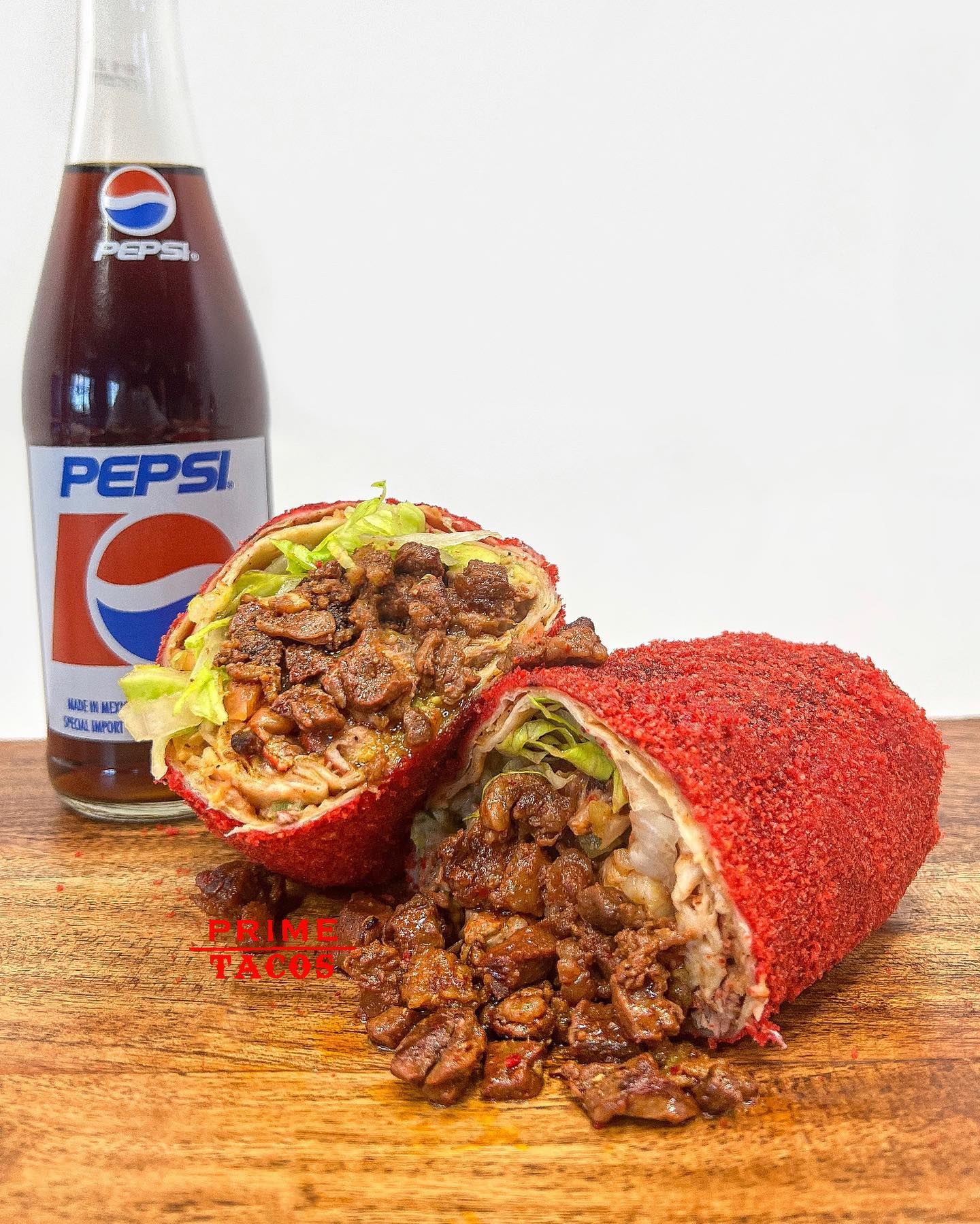 A Hot Cheeto burrito halved to show steak and lettuce, next to a glass bottle of Pepsi