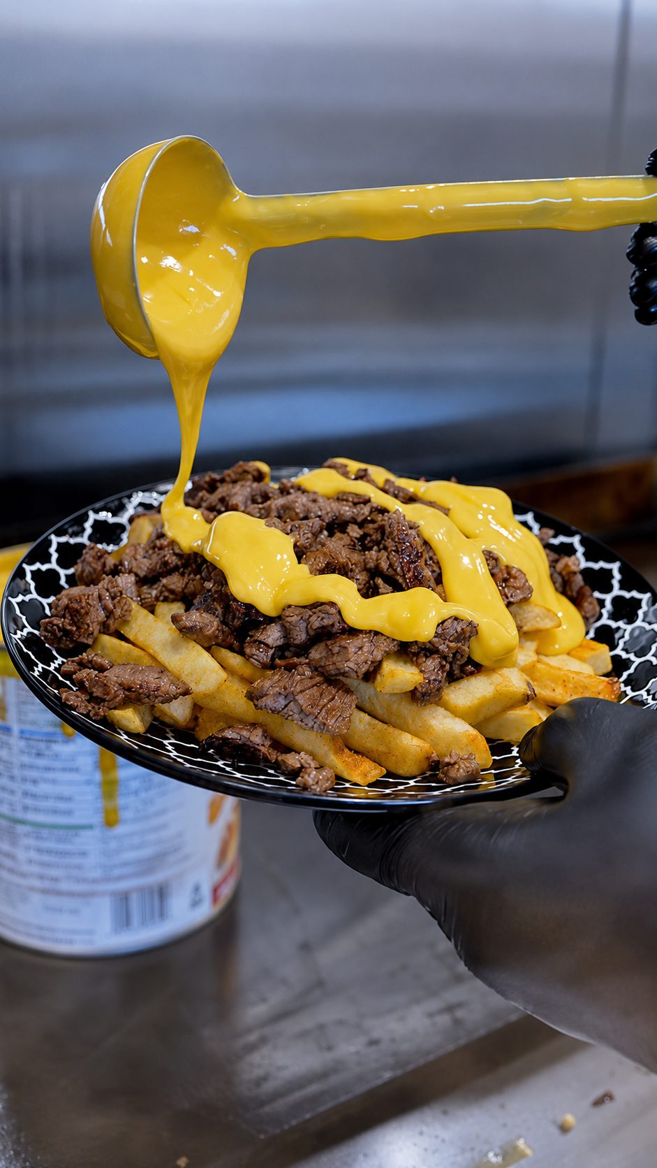 Nacho cheese being ladled over loaded fries topped with grilled steak
