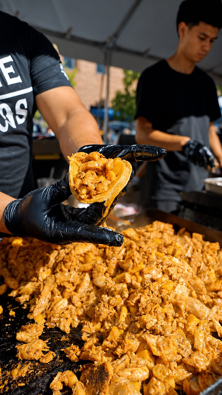 A gloved hand folding a chicken al pastor taco over a flat top piled with marinated chicken