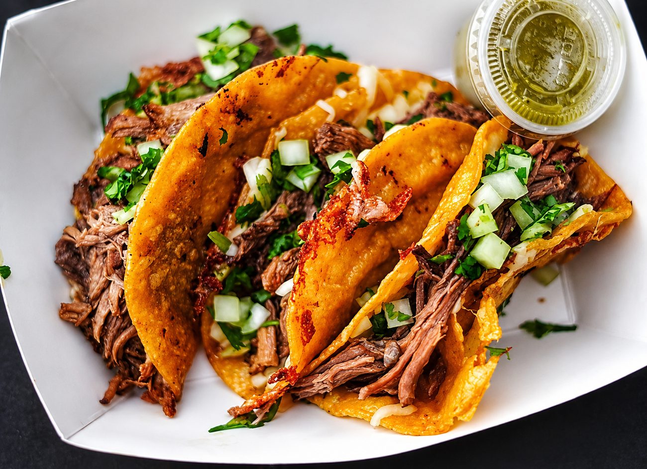A plate of quesabirria tacos with crisped cheese edges and a cup of salsa verde