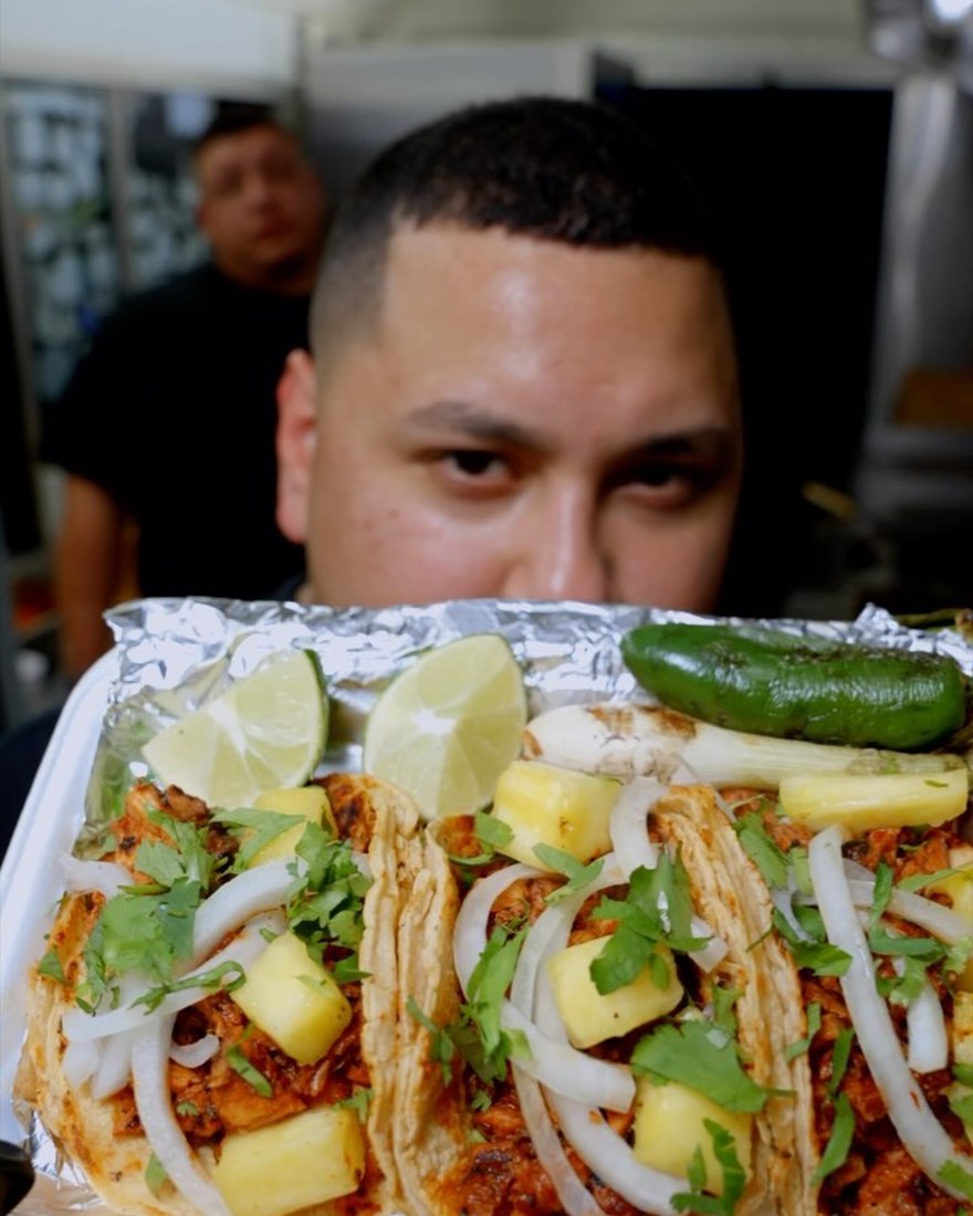 Eric Cardenas holding up a tray of chicken al pastor tacos with lime and grilled jalapeño